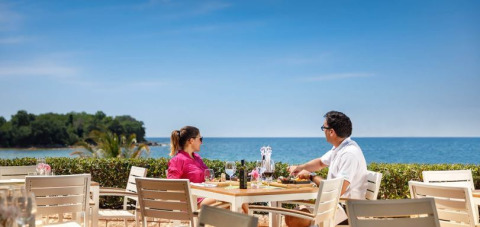 Paar genießt Mittagessen mit Meerblick auf Camping Aminess Maravea in Istrien, Kroatien bei klarem Himmel.