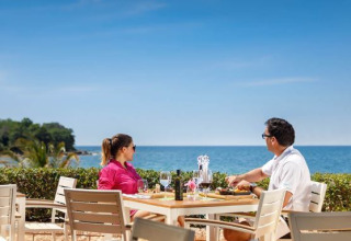 Par nyder frokost ved borde med havudsigt på Camping Aminess Maravea i Istrien, Kroatien under klar himmel.