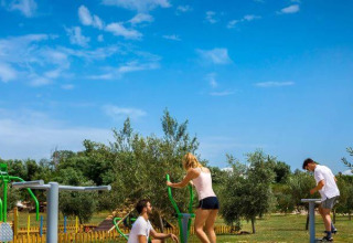 Folk træner udendørs på fitnessudstyr under en blå himmel i Camping Aminess Maravea, Istrien, Kroatien.