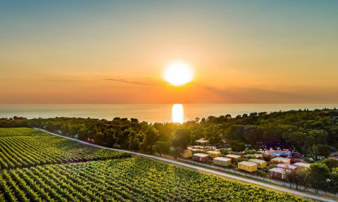 Tramonto al Camping Aminess Maravea in Istria, Croazia, con campi verdi, bungalow e il mare sullo sfondo.