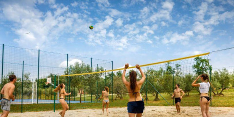 Junge Leute spielen Beachvolleyball unter blauem Himmel im Camping Aminess Maravea, Istrien, Kroatien.