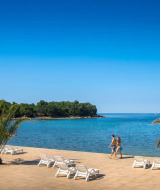 Vista de playa en Camping Aminess Maravea, Istria, Croacia, con palmeras, tumbonas y mar azul brillante.
