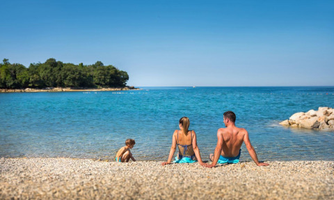 Famiglia rilassata sulla spiaggia di ciottoli davanti al mare blu al Camping Aminess Maravea, Istria, Croazia.
