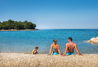 Famiglia rilassata sulla spiaggia di ciottoli davanti al mare blu al Camping Aminess Maravea, Istria, Croazia.