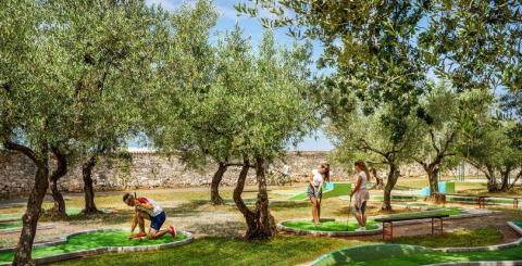 Villaggio turistico in Istria, Croazia, con persone che giocano a mini golf tra gli ulivi in una giornata di sole.
