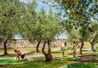 Villaggio turistico in Istria, Croazia, con persone che giocano a mini golf tra gli ulivi in una giornata di sole.