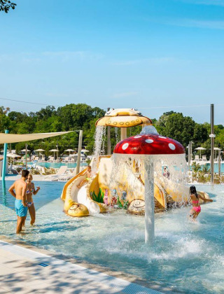 Niños divirtiéndose en la piscina interactiva con fuentes de setas en Camping Aminess Maravea, Croacia.