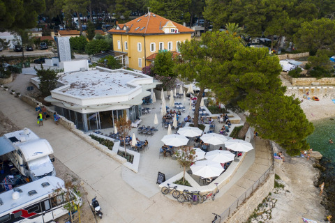 Vista aérea de una terraza y restaurante en Camping Cikat, Croacia, cerca de la costa y autocaravanas.