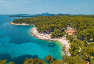 Luftfoto af Camping Cikat i Primorje-Gorski Kotar, Kroatien, med blå bugt, strand og fyrretræer.