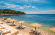 Strand med liggestole og parasoller ved Camping Cikat, Primorje-Gorski Kotar, Kroatien, under blå himmel.