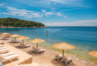 Sun loungers and straw umbrellas on the beach at Camping Cikat, Primorje-Gorski Kotar County, Croatia.