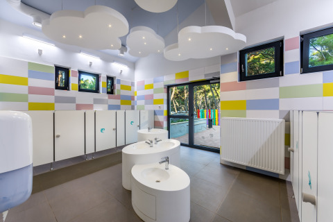 Baño infantil con paredes de colores, luces de techo en forma de nube y lavabos redondos en Camping Cikat.