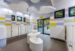 Salle de bains pour enfants aux murs colorés, luminaires nuages et lavabos ronds au Camping Cikat.
