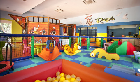 Parque infantil interior en Camping Cikat con juegos coloridos, piscina de bolas y decoración de barco pirata.
