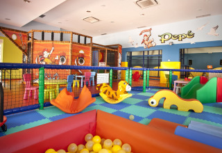 Parque infantil interior en Camping Cikat con juegos coloridos, piscina de bolas y decoración de barco pirata.