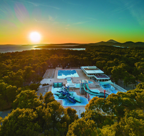 Vista del atardecer en Camping Cikat en Croacia con piscinas, toboganes de agua y bosque alrededor.