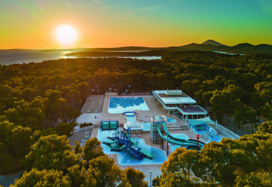Solnedgang over Camping Cikat feriepark med pool og vandrutsjebaner omgivet af skov i Kroatien.