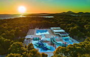 Sonnenuntergang über dem Camping Cikat Ferienpark mit Pools und Rutschen, umgeben von Wald in Kroatien.