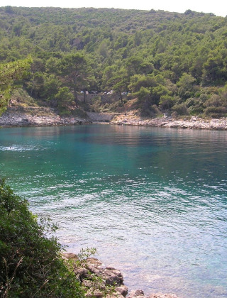 Vista de una bahía tranquila con agua azul cristalina y colinas boscosas cerca de Mali Lošinj, Croacia.
