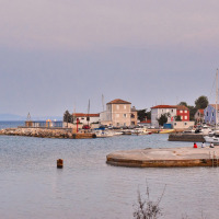 Puerto cerca de Mali Lošinj, Croacia, con barcos, casas coloridas y el mar tranquilo al atardecer.