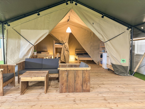Tente safari avec mobilier en bois, coin salon, lit et kitchenette sur un plancher en bois.