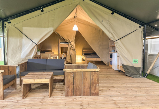 Tente safari avec mobilier en bois, coin salon, lit et kitchenette sur un plancher en bois.