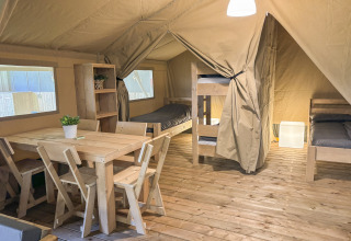Interieur van een safaritent bij Toftum Bjerge Camping in Denemarken met houten meubels en stapelbedden.