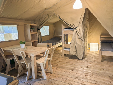 Interior de tienda safari en Toftum Bjerge Camping, Dinamarca, con muebles de madera y literas.