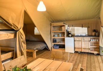 Safari-Zelt-Innenraum mit Etagenbett, Doppelbett, Esstisch und voll ausgestatteter Küche auf Holzboden.