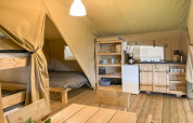 Interior de tienda safari con litera, cama doble, mesa de comedor y cocina totalmente equipada en suelo de madera.