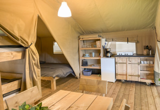 Interior de tienda safari con litera, cama doble, mesa de comedor y cocina totalmente equipada en suelo de madera.