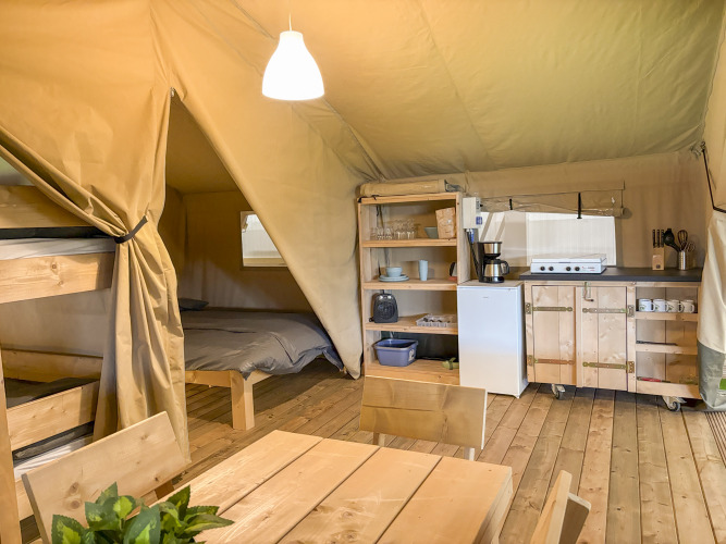 Safari tent interior with bunk bed, double bed, dining table, and fully equipped kitchen on wooden floor.