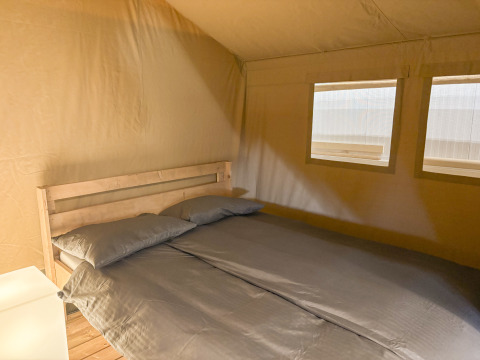Vista interior de una tienda safari con cama doble y dos ventanas en Toftum Bjerge Camping, Dinamarca.
