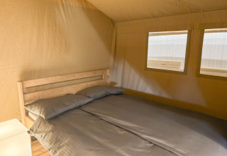 Interior view of a safari tent with a double bed and two windows at Toftum Bjerge Camping, Denmark.