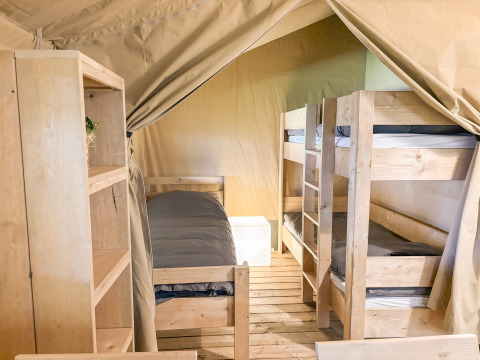 Interior de una tienda safari en Toftum Bjerge Camping en Dinamarca con literas y estanterías de madera.