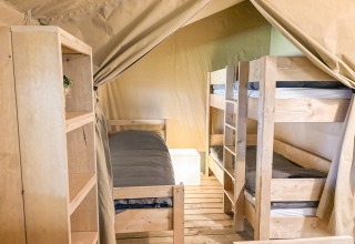 Interior de una tienda safari en Toftum Bjerge Camping en Dinamarca con literas y estanterías de madera.