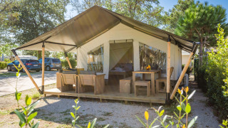 Tenda safari Comfort con aria condizionata, veranda con arredi in legno su campeggio soleggiato.