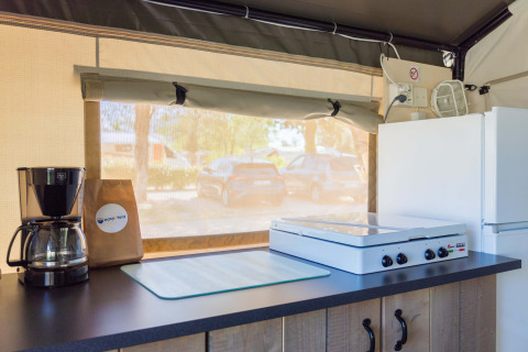 Angolo cucina interno in tenda safari con macchina da caffè, fornello e frigo al Camping Stella Maris.