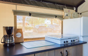Binnenkeuken van een safaritent met koffiezetapparaat, kookplaat en koelkast bij Camping Stella Maris.