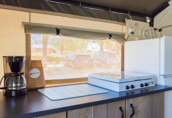 Angolo cucina interno in tenda safari con macchina da caffè, fornello e frigo al Camping Stella Maris.