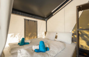 Interior of a safari tent bedroom with a double bed, white bedding, and turquoise towels on top.