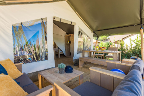 Innenraum eines Safari-Zeltes mit Holzsofas, Kissen und Esstisch, grüner Außenbereich sichtbar.