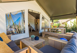 Interieur van een safaritent met houten zitbanken, eethoek en zicht op groene buitenomgeving.