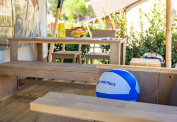 Terraza exterior con bancos de madera, mesa y balón playero en Safari tent Comfort, Camping Stella Maris Croacia.