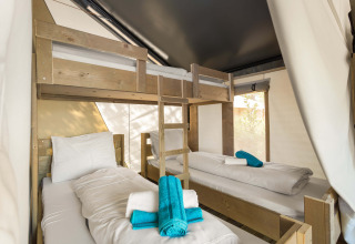 Vista interna di una tenda safari con un letto a castello e due singoli, biancheria bianca e asciugamani blu.