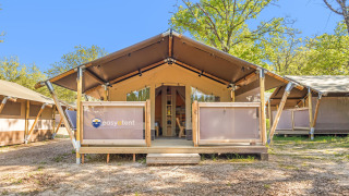 Tenda Safari Cozy su veranda in legno in campeggio, circondata da alberi e cielo sereno.
