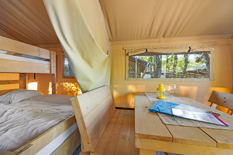 Interior of Safari Tent Lodge at Camping Cikat, Croatia, with bed, bunk bed, wooden table and benches.