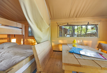 Interior of Safari Tent Lodge at Camping Cikat, Croatia, with bed, bunk bed, wooden table and benches.