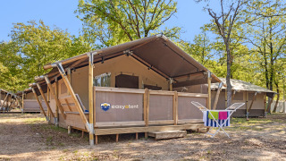 Lodge de tienda safari en un camping arbolado con porche y tendedero con toallas coloridas al frente.