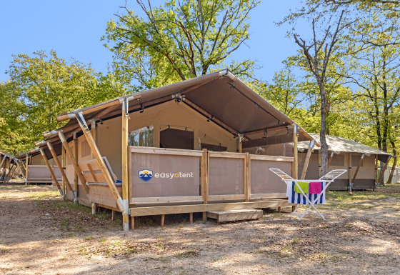 Lodge de tienda safari en un camping arbolado con porche y tendedero con toallas coloridas al frente.